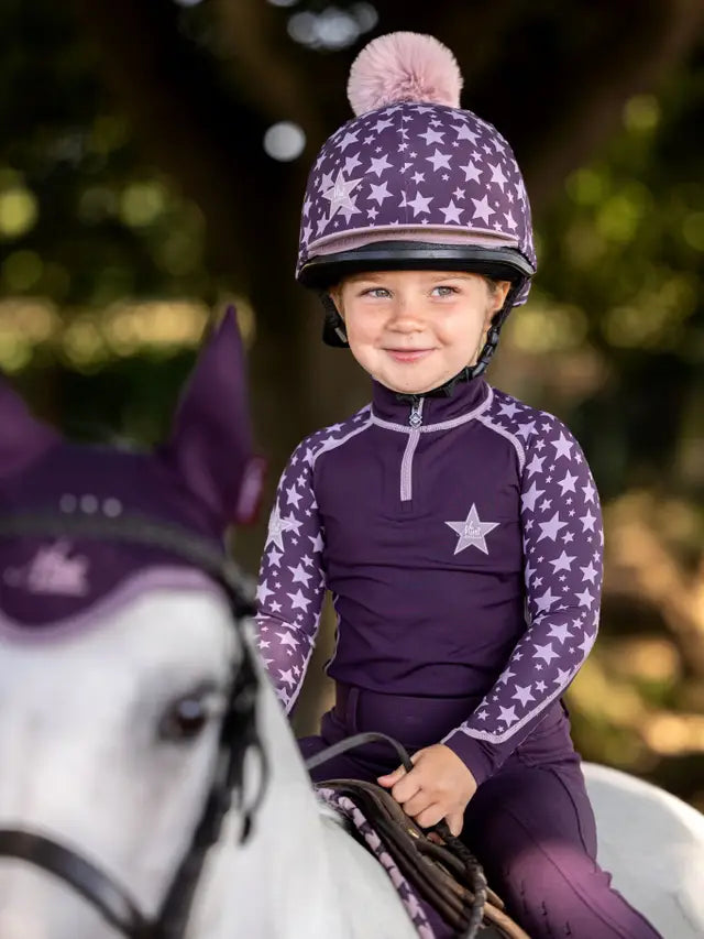 LeMieux Mini Base Layer Fig: Girl riding horse in star-patterned top & helmet. Comfortable child riding gear by Equiflair.