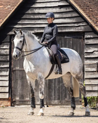 LeMieux Dressage Work Pad Black: Woman riding gray horse with LeMieux dressage pad in black. Comfortable horse riding and schooling gear.
