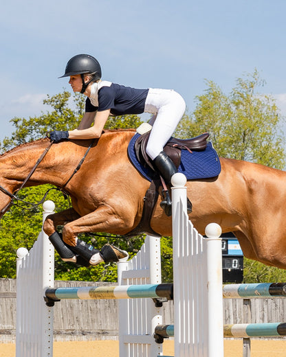 Horse jumping with rider using Woof Wear navy dressage sheepskin saddle pad. Equestrian sport.