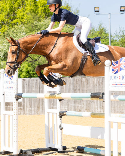 Chestnut horse jumping obstacle in show jumping competition. Equestrian athlete. WOOF WEAR sheepskin pad.