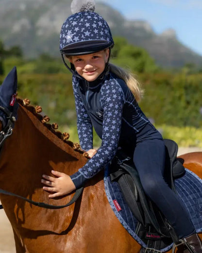 Girl riding horse wearing LeMieux Mini Hat Silk Indigo with star design. Equestrian kids' apparel from Equiflair.