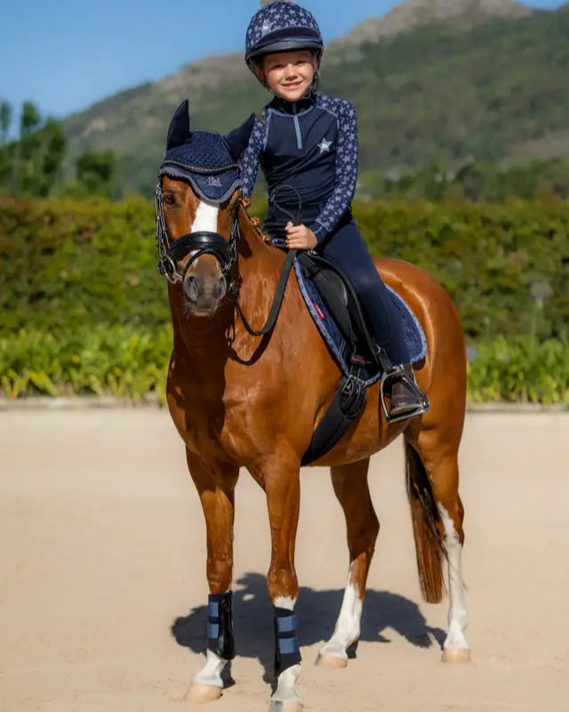 Child rider on pony wearing LeMieux Mini Fly Hood Indigo. Equestrian horse riding gear for small ponies. Indigo pony fly mask.