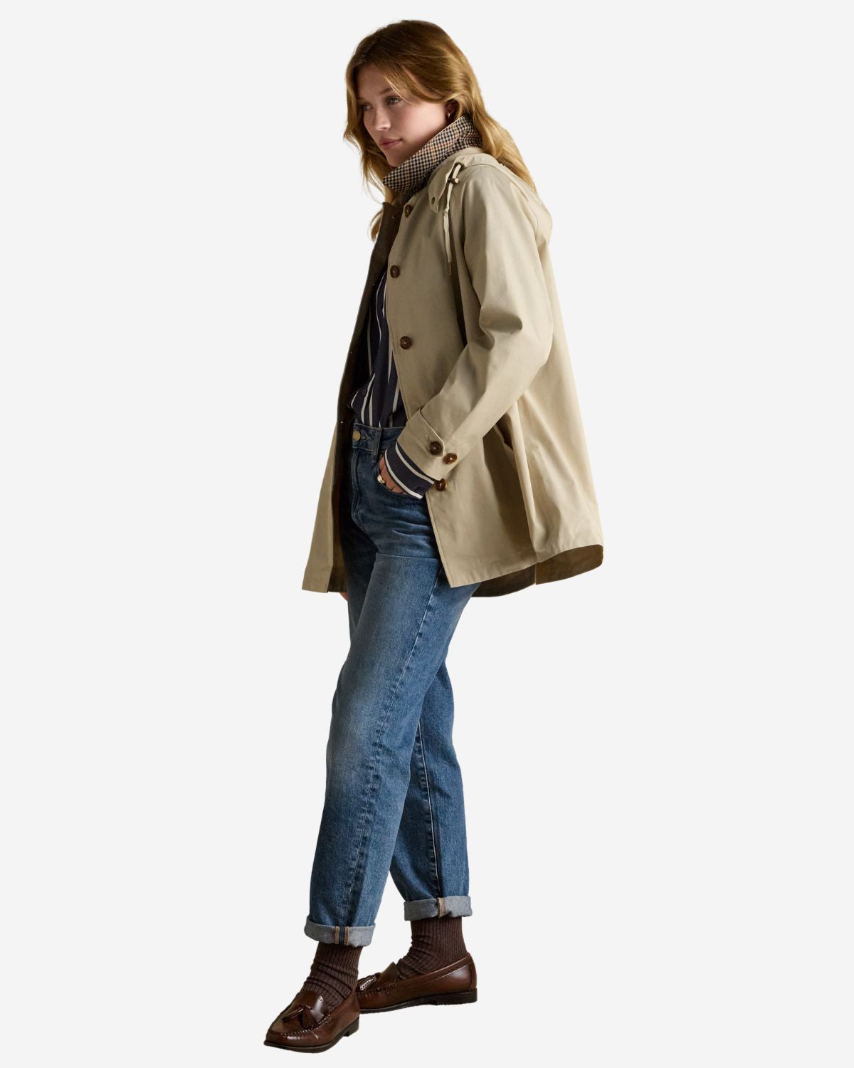 Joules Rainmore Waterproof Raincoat: Neutral button-up women's jacket with hood, blue jeans, and brown loafers.