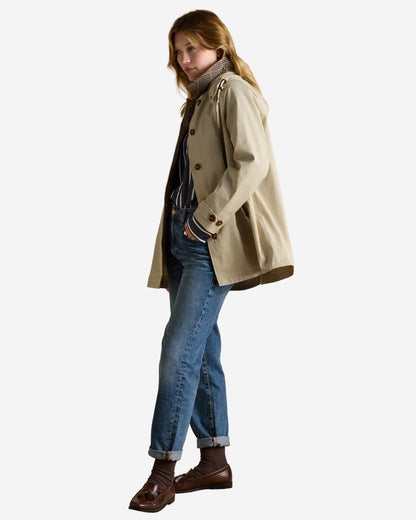 Joules Rainmore Waterproof Raincoat: Neutral button-up women's jacket with hood, blue jeans, and brown loafers.
