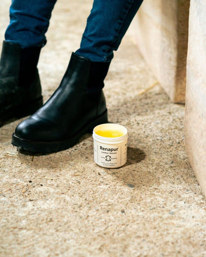 Renapur Leather Balsam jar next to black leather boots and denim jeans. Shop at Equiflair.