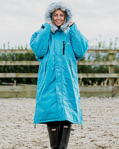 EQUIDRY Evolution Lux Women's Warm Waterproof Winter Horse Riding Coat Thick Fleece Lining with Faux Fur Trim Hood in turquoise rider stood with hood up