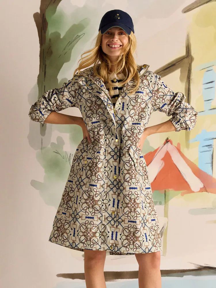 JOULES HOLKHAM Horse Tack Stone Waterproof Packable Raincoat. Stylish woman in patterned raincoat with navy cap smiling.