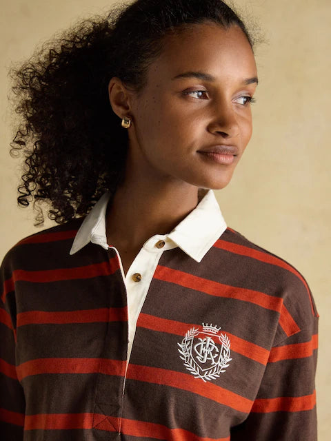 JOULES Lara Red & Brown Striped Rugby Shirt. Woman wearing long sleeve cotton boxy fit rugby top with crest logo. Casual fashion style.