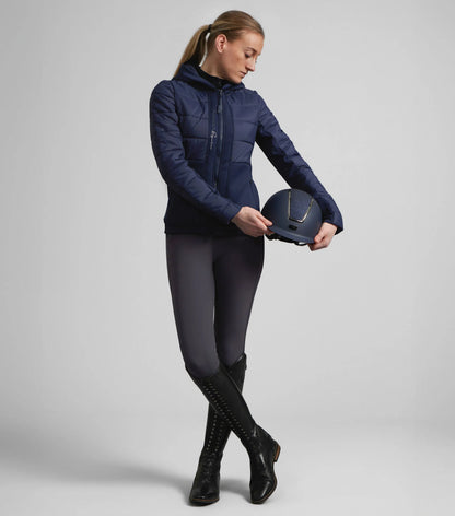 Premier Equine Agata Ladies Riding Jacket Navy: Equestrian woman holding helmet. Quilted, hooded riding jacket for women.