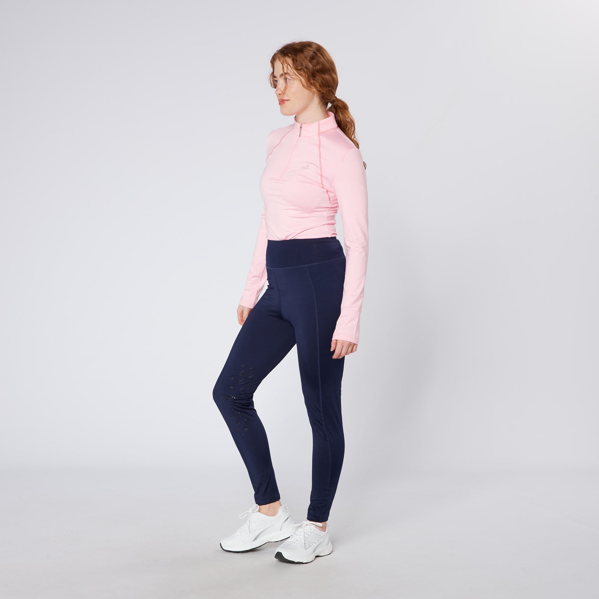 Equiflair Cameo Pink Baselayer & Riding Leggings. Equestrian woman in long sleeve quarter zip pink top and navy athletic leggings.