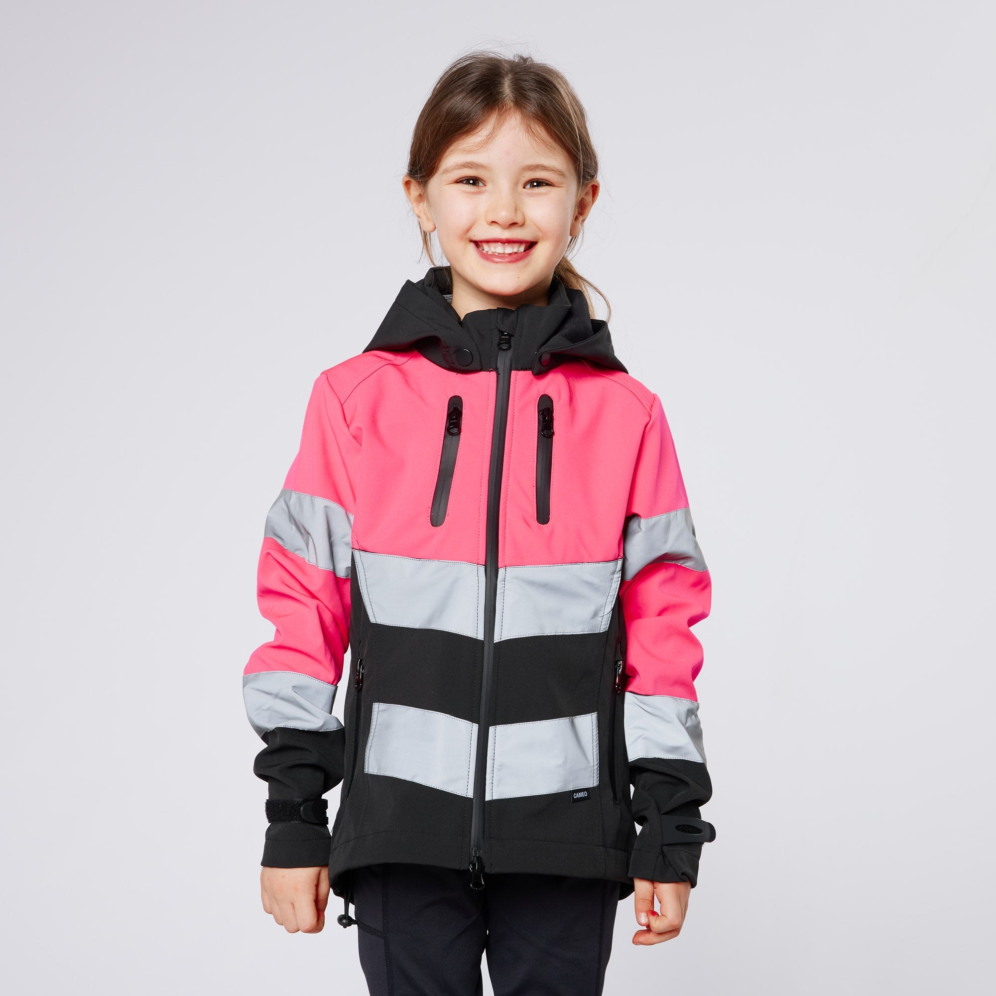 Smiling girl wearing a pink, black, and gray Cameo Junior Hi Viz Jacket with hood against a white background.