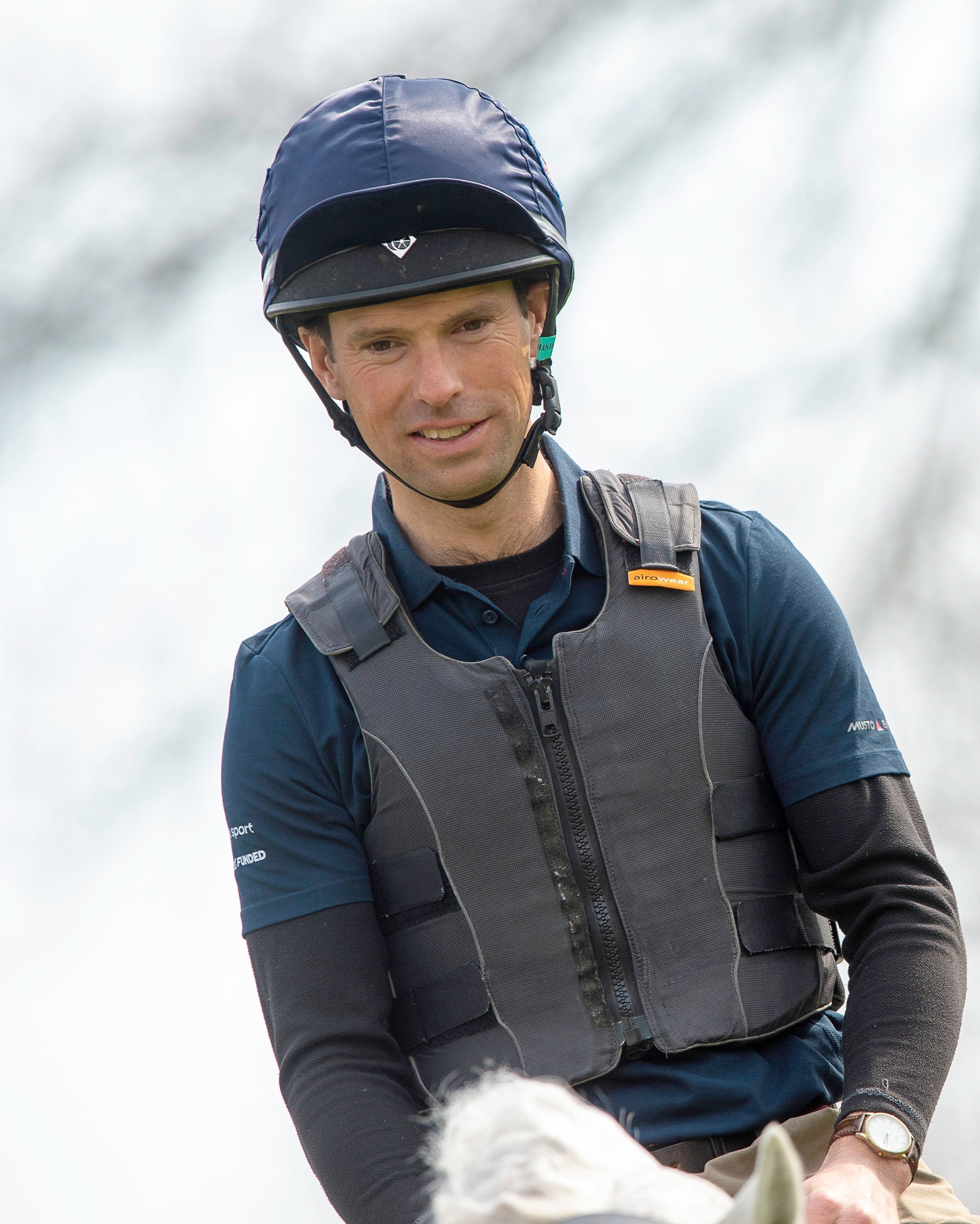 Equestrian rider wearing a Charles Owen Pro II Plus Jockey Skull Navy helmet and safety vest on horseback.