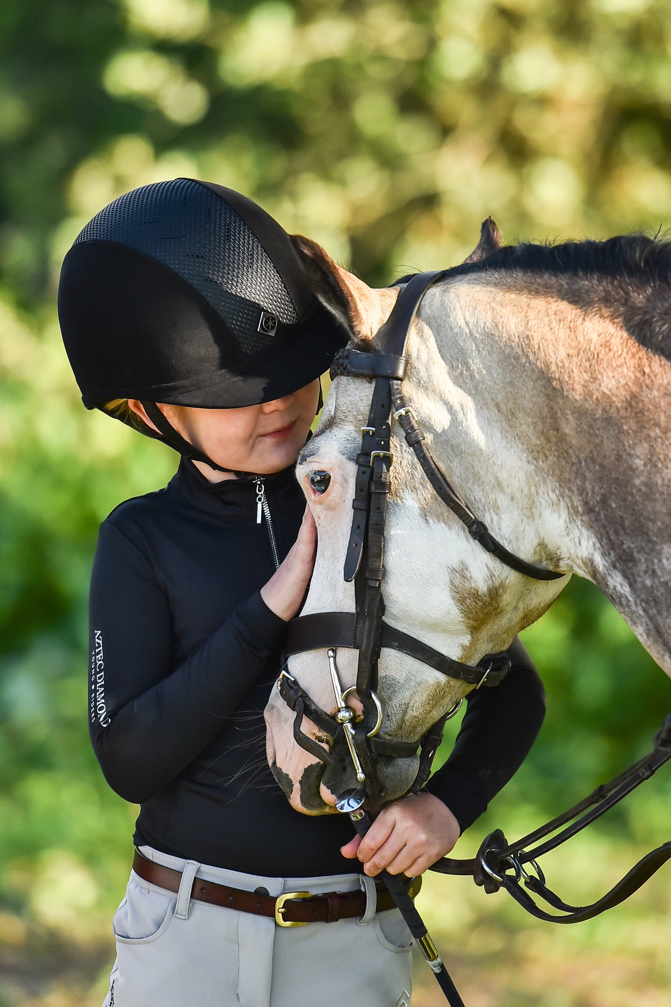 Girl hugging horse wearing Charles Owen AYR8 Plus helmet. Equestrian rider safety gear.
