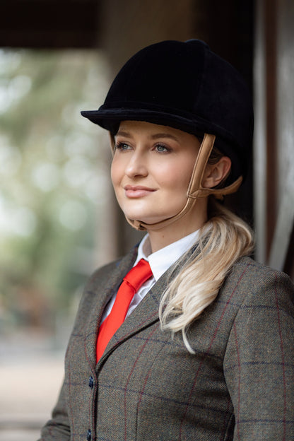 Equestrian portrait: woman in Charles Owen riding helmet, tweed jacket, and red tie. Elegant, safe equestrian style by Equiflair.