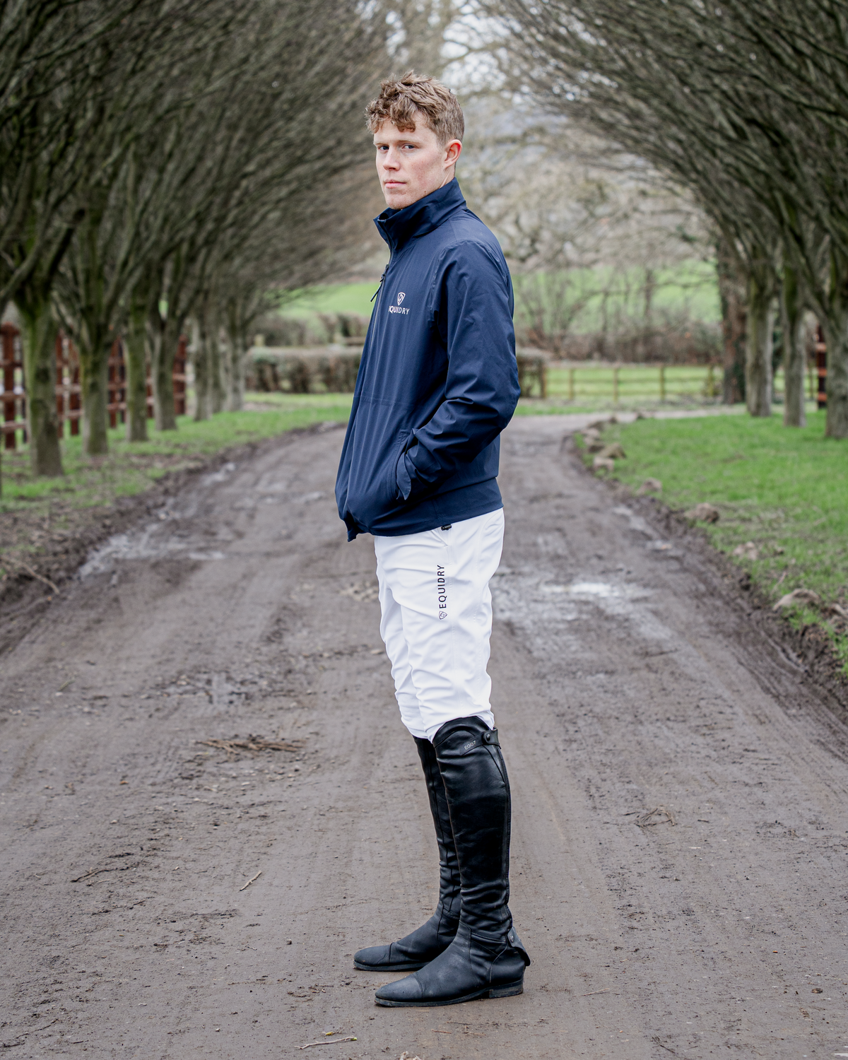 Men's Equidry white waterproof riding breeches and black boots in an equestrian outdoor setting.
