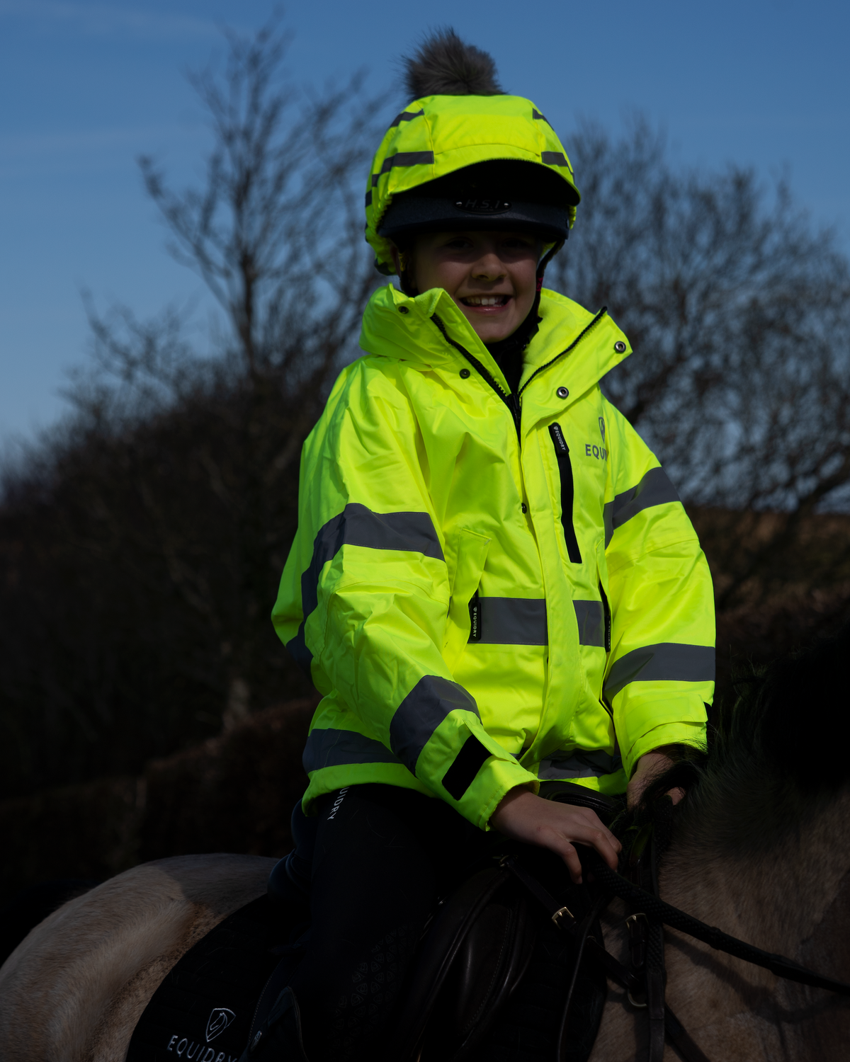 Child in hi-vis yellow Equidry horse riding jacket and helmet, bright & safe for equestrian adventures.