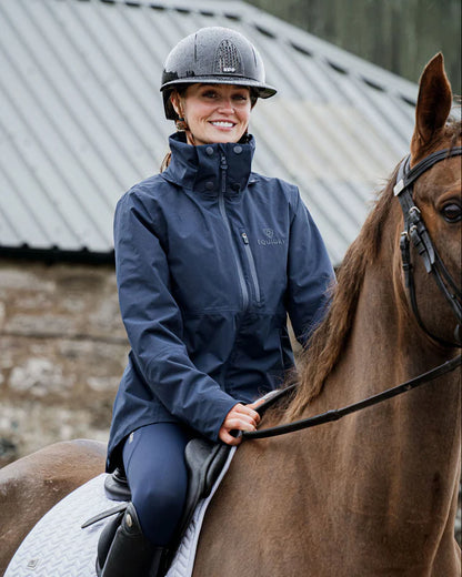 Equidry IRIS Waterproof Riding Jacket for Women in Navy. Woman riding a horse in a navy riding jacket and helmet.