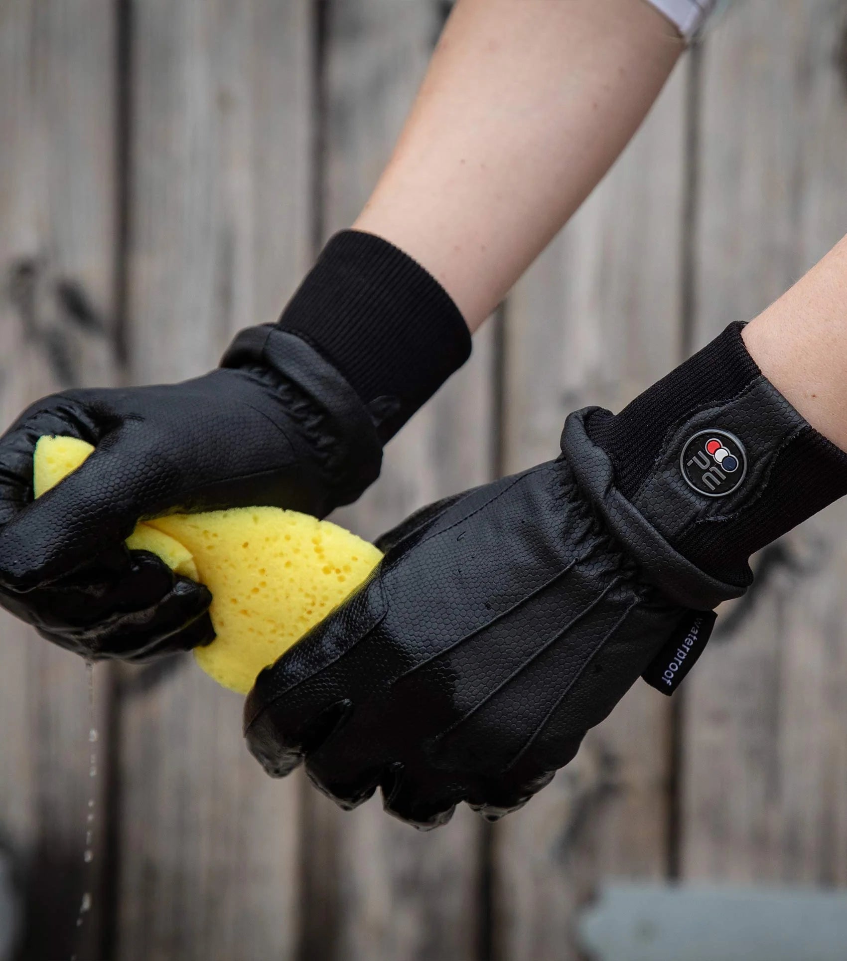 Premier Equine Waterproof Riding Gloves Black - Hands with wet sponge, close-up view. Waterproof gloves, riding gear, equestrian