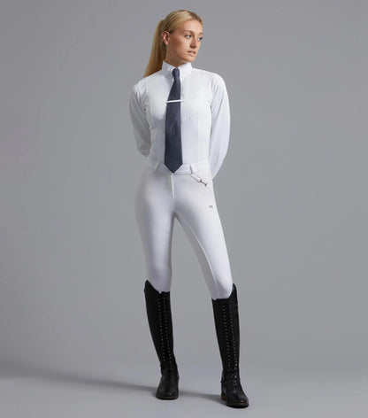 Woman in Premier Equine Delta White Breeches, Full Seat Gel, Equestrian Style, riding boots, shirt and tie posing in grey background