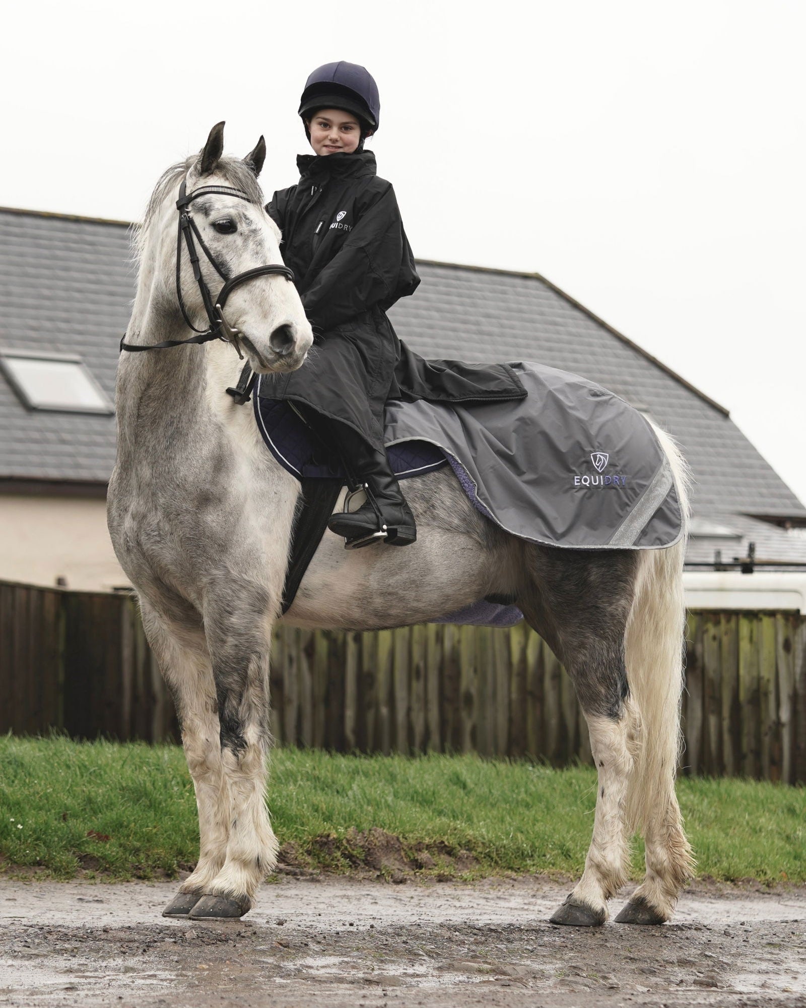Girl in Equidry horse riding coat. Waterproof children's equestrian jacket, black, fleece lined with stowaway hood.