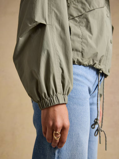Joules Hove Khaki Green Waterproof Windbreaker Jacket. Woman wearing the jacket, showcasing sleeve and modern ring.