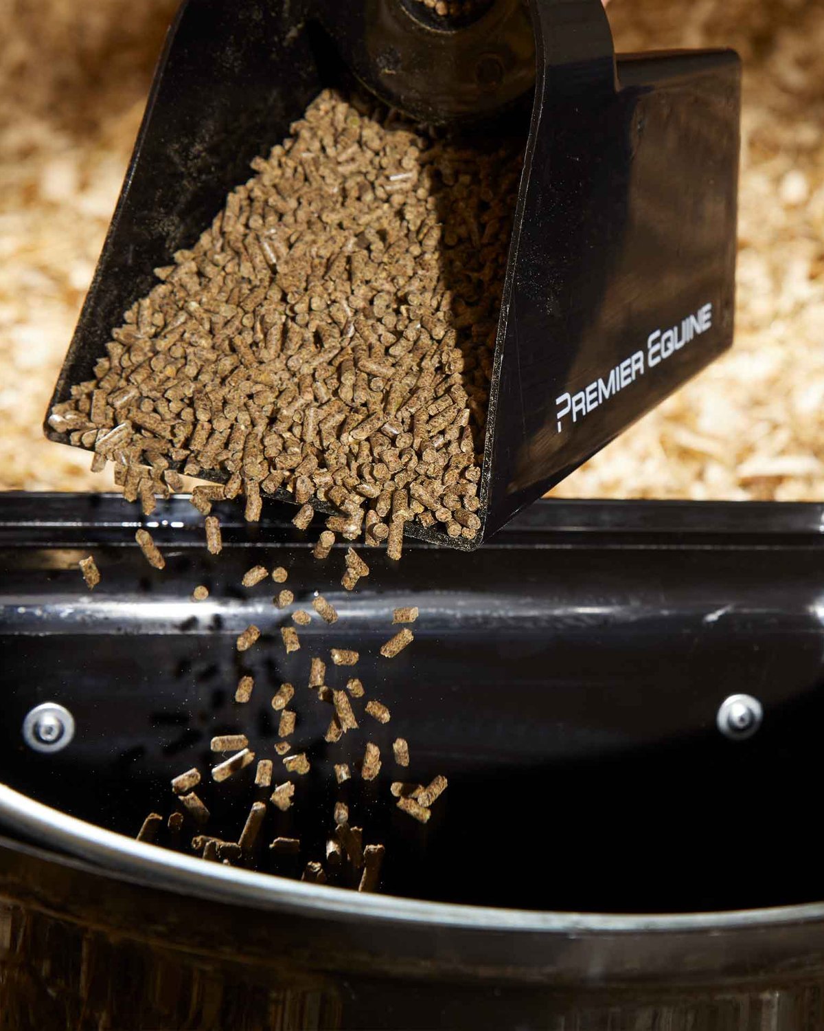 Horse Feed Pellets Being Poured from a Black PREMIER EQUINE Scoop into a Feeder Tub