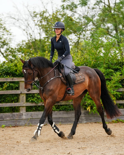 Equestrian: Woman riding horse with Woof Wear Vision Elegance Tendon Boots. Outdoor setting.