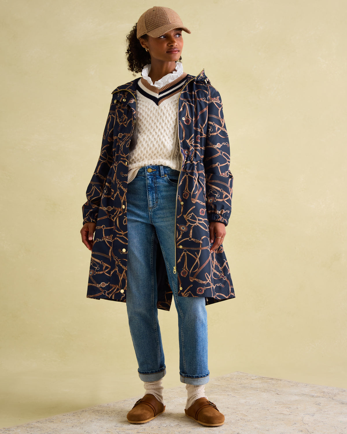 JOULES Holkham Navy Blue Waterproof Packable Raincoat. Woman in patterned coat, jeans and cap.
