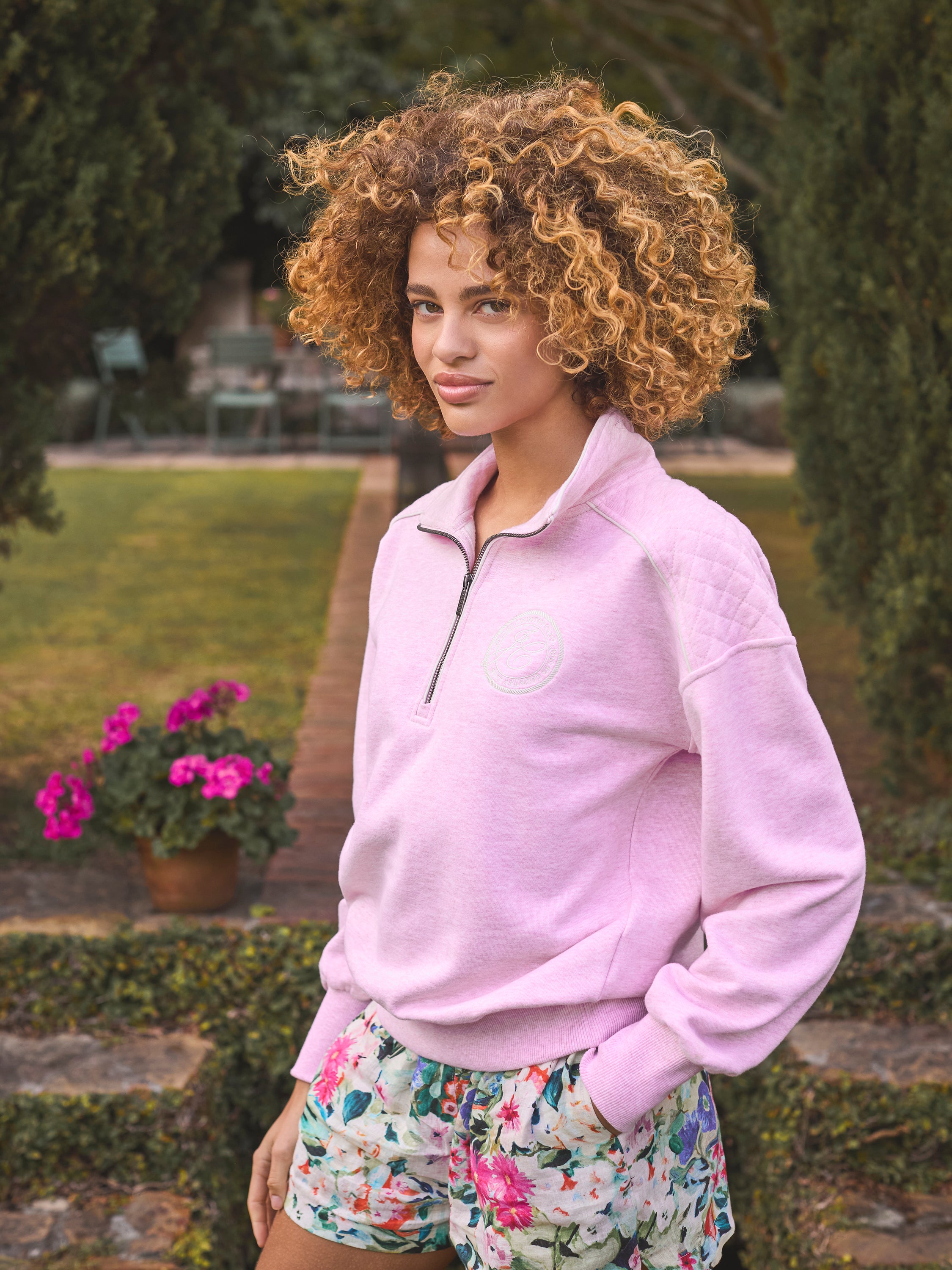Joules Racquet Half Zip Sweatshirt Pink: Woman in pink sweatshirt and floral shorts. Equiflair