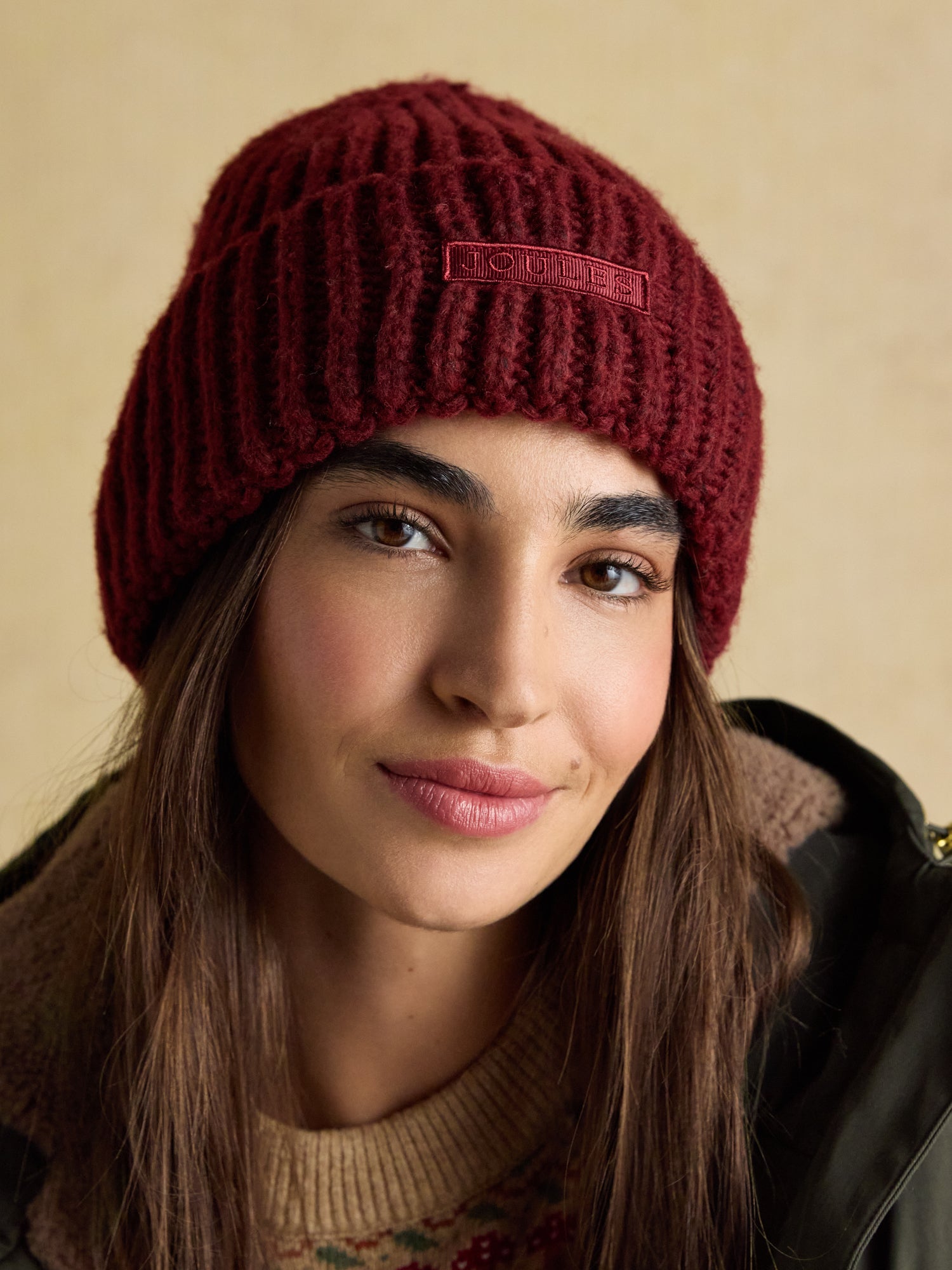 Red Joules Rosa Beanie knit hat, woman wearing winter fashion beanie with Joules logo.
