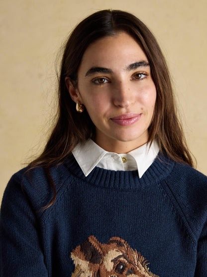 Woman wearing a JOULES Intarsia Monty Dog Cotton Blend Jumper, a fun crew neck sweater with a dog design and gold earrings.