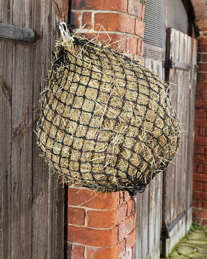 Hay Net for Horses: Black Mesh Haylage Feeder Filled with Hay Hanging on Wood and Brick | Horse Feeding Supplies