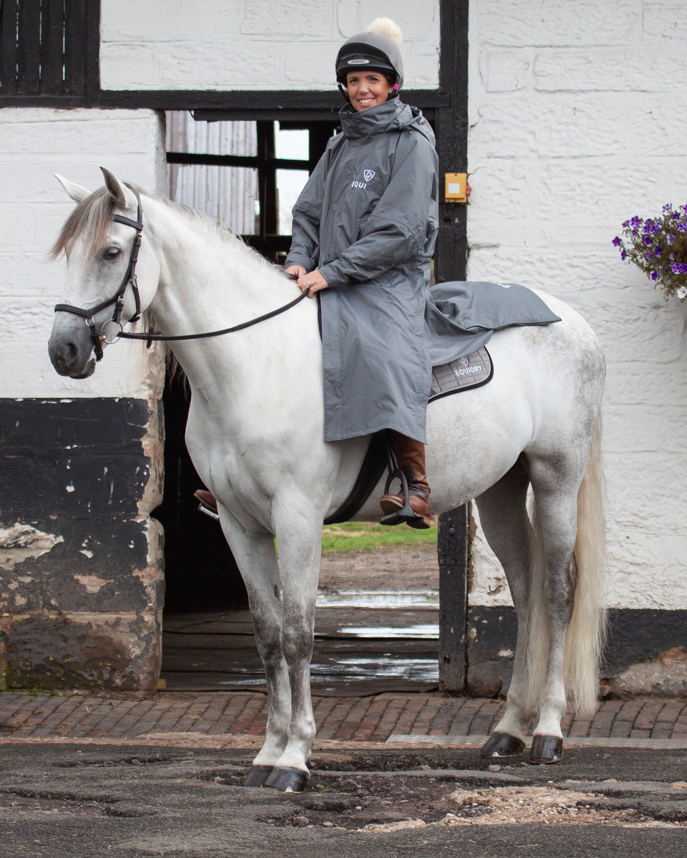 Woman on horse wearing an EQUIDRY grey equestrian waterproof riding coat. Equiflair store image.