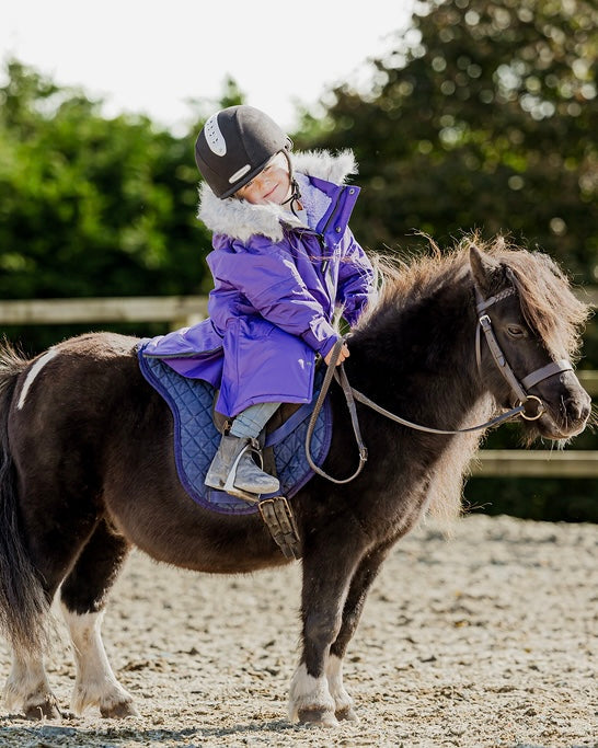 Child riding pony in EQUIDRY purple fleece coat, horseback riding.