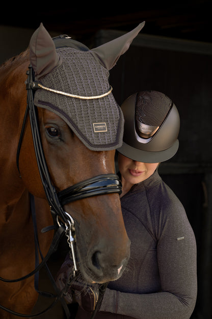 Brown horse wearing LeMieux cocoa fly hood, rider in helmet with herringbone pattern