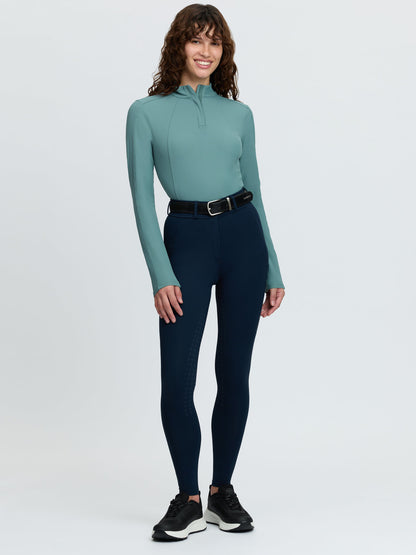Woman wearing LeMieux Becca Half Seat Breeches in Navy blue with a teal long sleeve shirt and black sneakers.