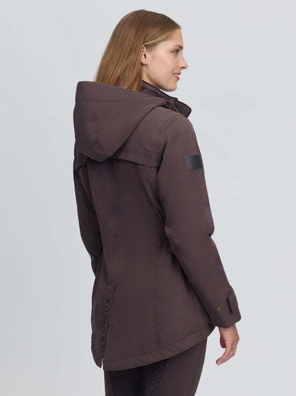 Woman wearing a cocoa brown LeMieux Heritage Beatrice waterproof coat with hood, side waist detail and riding vents.