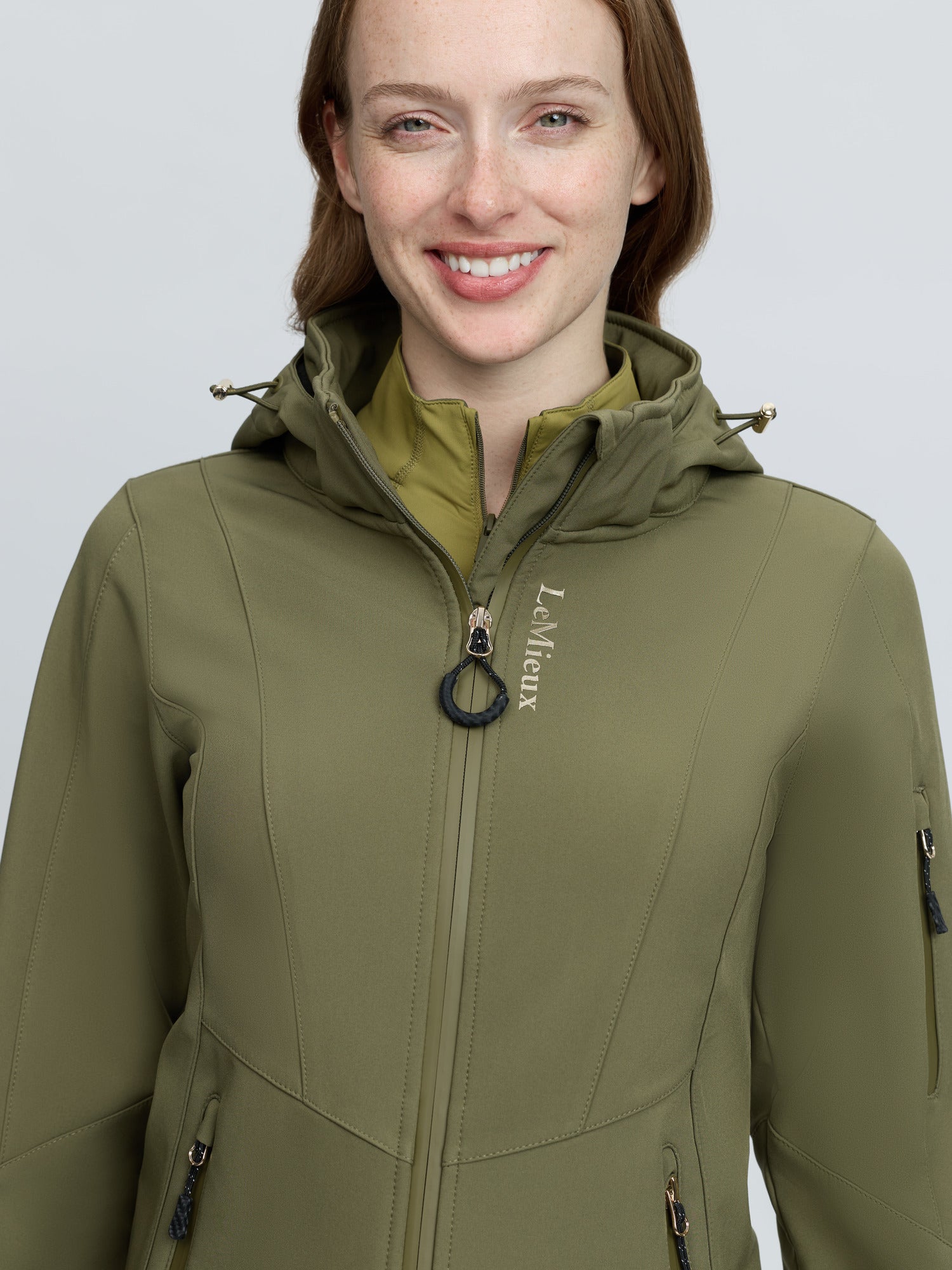 Woman in LEMIEUX CELINE SOFTSHELL JACKET in Willow Green, featuring a hood and zipper.