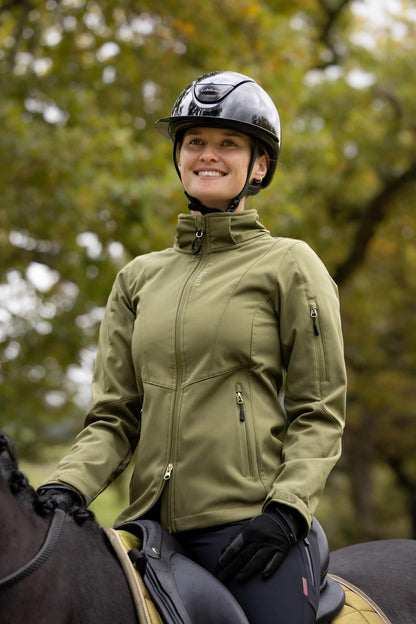 Equestrian woman in green LeMieux softshell jacket riding a horse, outdoor scene.