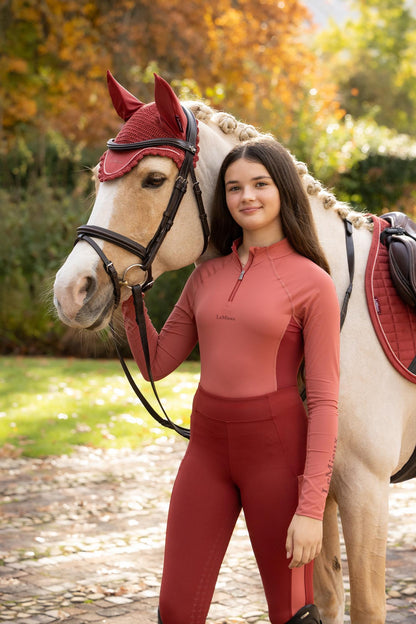 Young equestrian rider and horse in matching "Spiced Earth" red LeMieux Classique Collection gear outdoors.