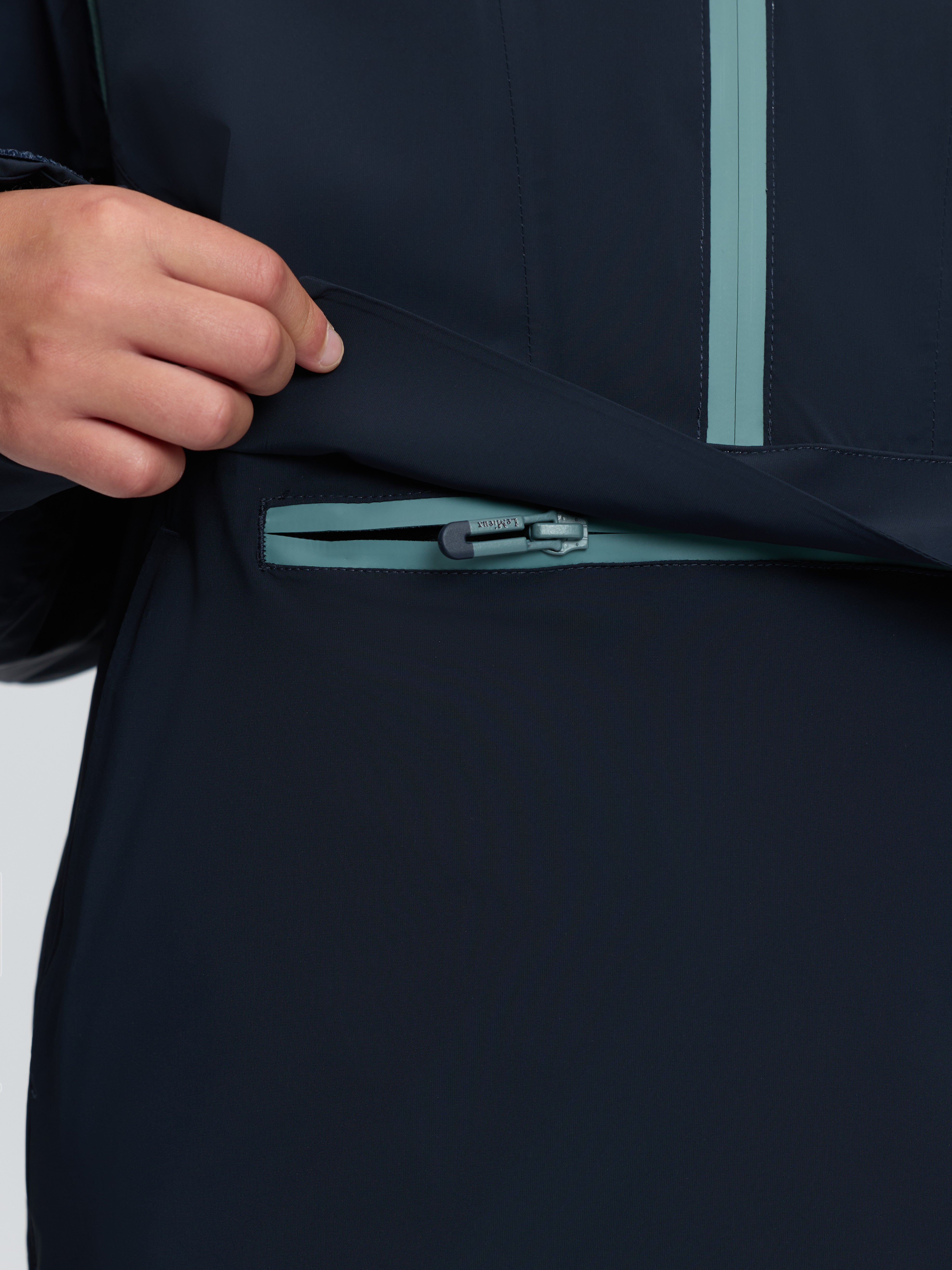 Close-up of navy blue LeMieux anorak kangaroo pocket with teal waterproof zipper and hand.