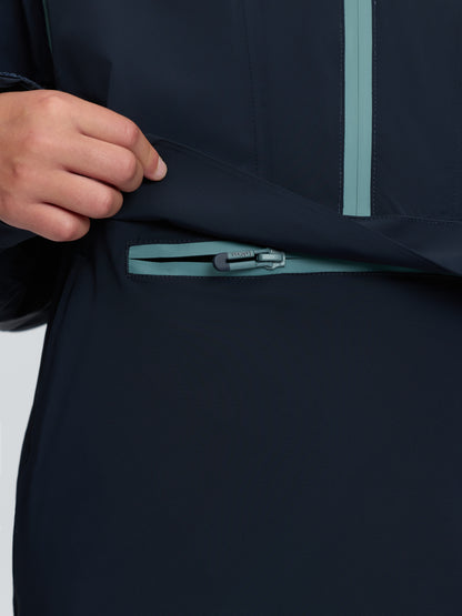 Close-up of navy blue LeMieux anorak kangaroo pocket with teal waterproof zipper and hand.