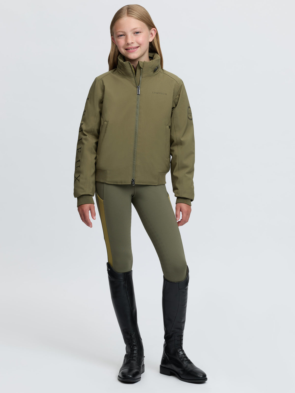 Young equestrian rider in stylish green Lemieux jacket and breeches, ready for competition.