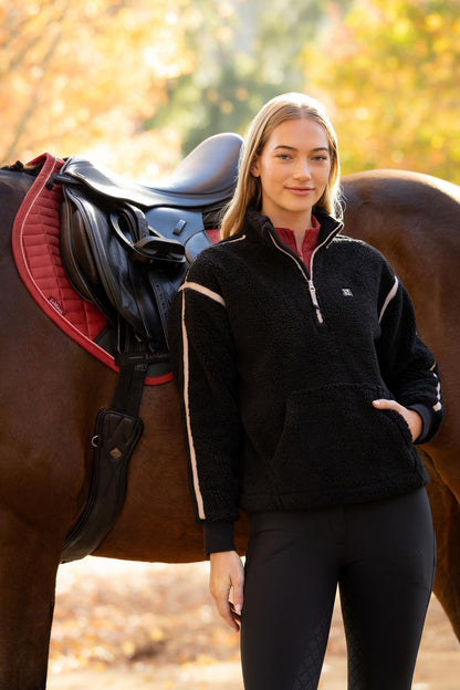 Woman in black LeMieux Avery Teddy Quarter Zip Fleece posing with a horse and saddle. Equestrian style.
