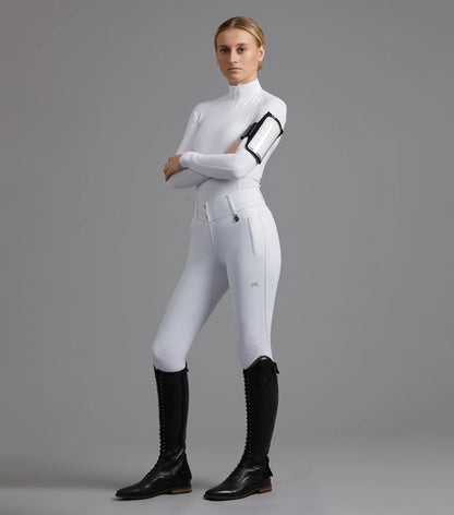 Equestrian woman in white riding outfit showcasing a Premier Equine Sport medical armband for horse riding.