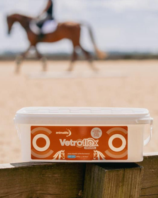 Animalife Vetroflex Original Horse Joint Supplement Tub on Fence with Horse Rider in Background