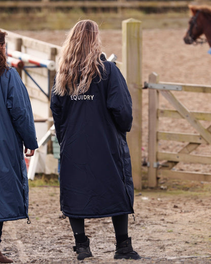 EQUIDRY women's long waterproof horse riding coat in navy/cream mums stood spectating riding lesson by arena, back of coats 