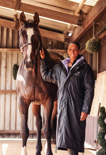 EQUIDRY women's long waterproof horse riding coat in Black/Lilac rider on yard with horse