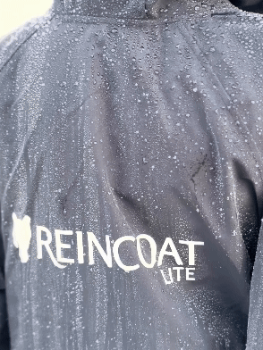 REINCOAT Waterproof Jacket: Close-up of rain-resistant material with water droplets, showcasing the brand's logo.