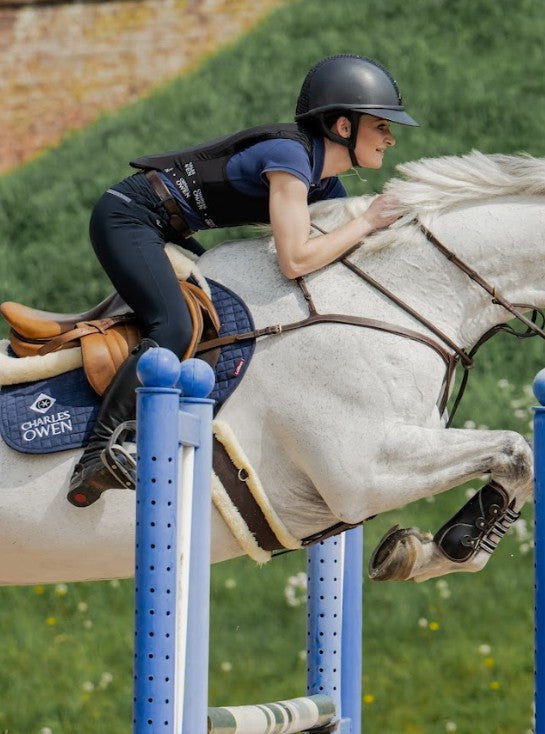 Equestrian show jumping: Rider wearing Charles Owen Shadow back protector for safety. Horse and rider clearing a jump.